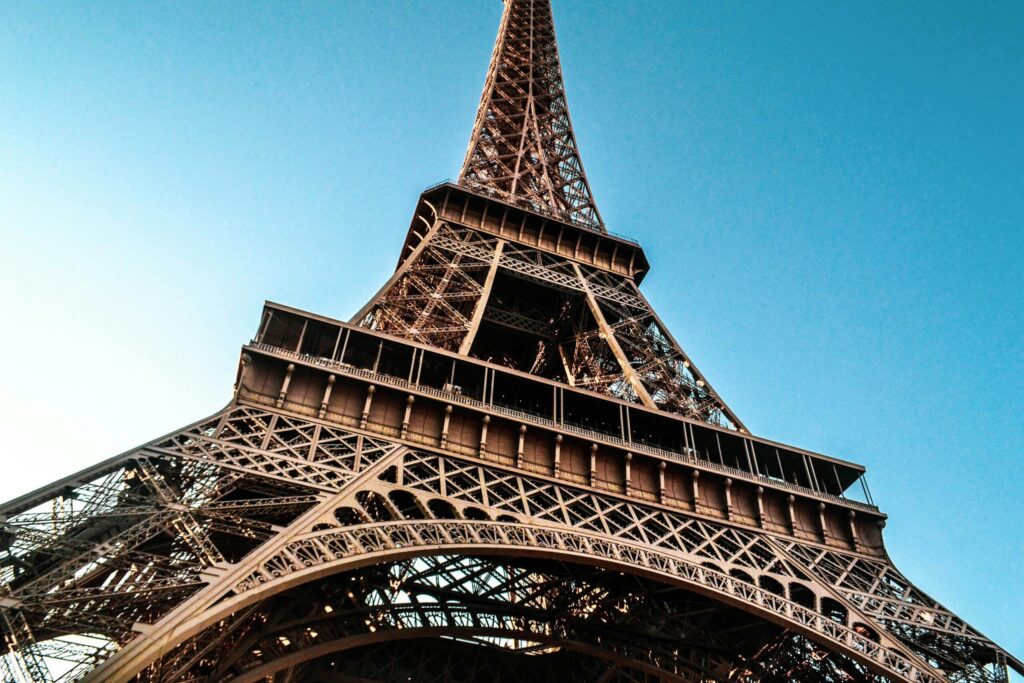 An iconic view of the Eiffel Tower from a low angle, highlighting its intricate iron lattice structure against a clear blue sky.