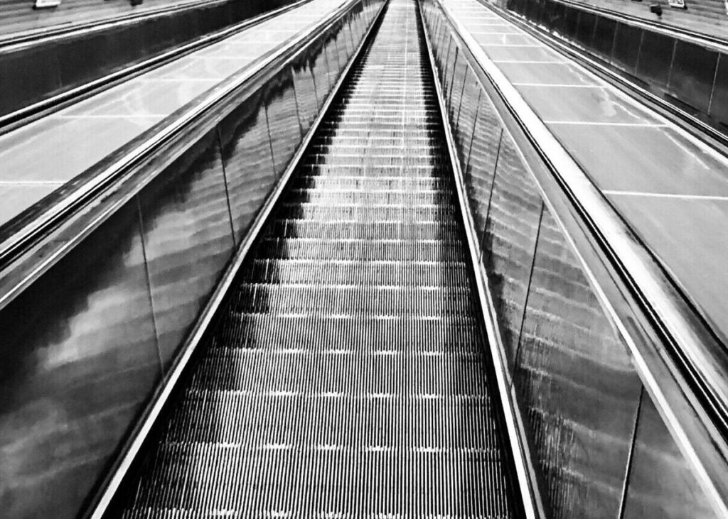 Black and white photo of an underground escalator with a lone commuter, emphasizing urban transportation.